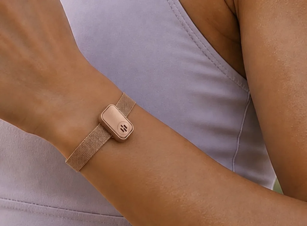 Wrist-worn smartwatch with rose gold finish and mesh band on person wearing lavender clothing.