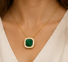 Woman wearing gold chain necklace with emerald green stone pendant surrounded by diamond halo.